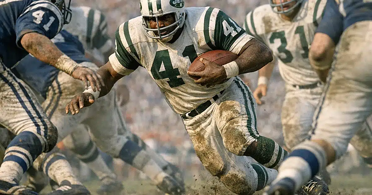 Running back in 1960s Jets uniform carrying football through defensive line at Super Bowl III