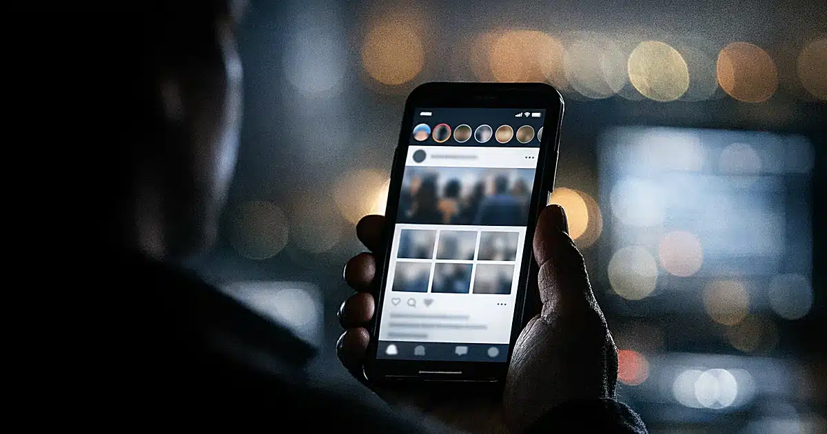 Silhouetted hand holding smartphone with glowing social media interface in dark setting