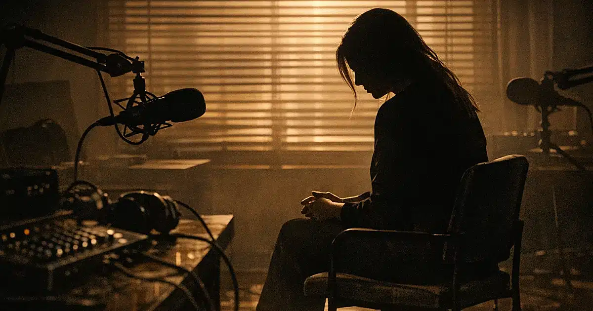 Silhouetted figure seated in dimly lit podcast studio with warm backlighting and recording equipment