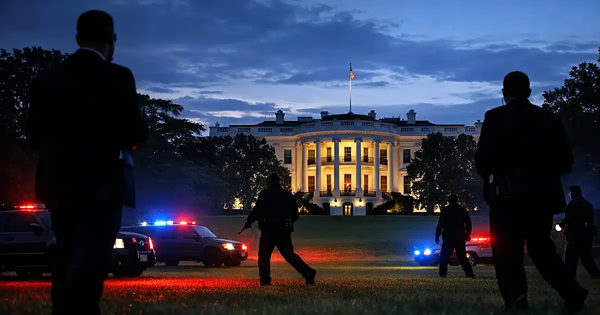 Secret Service agents silhouetted on White House South Lawn at dusk with emergency vehicle lights