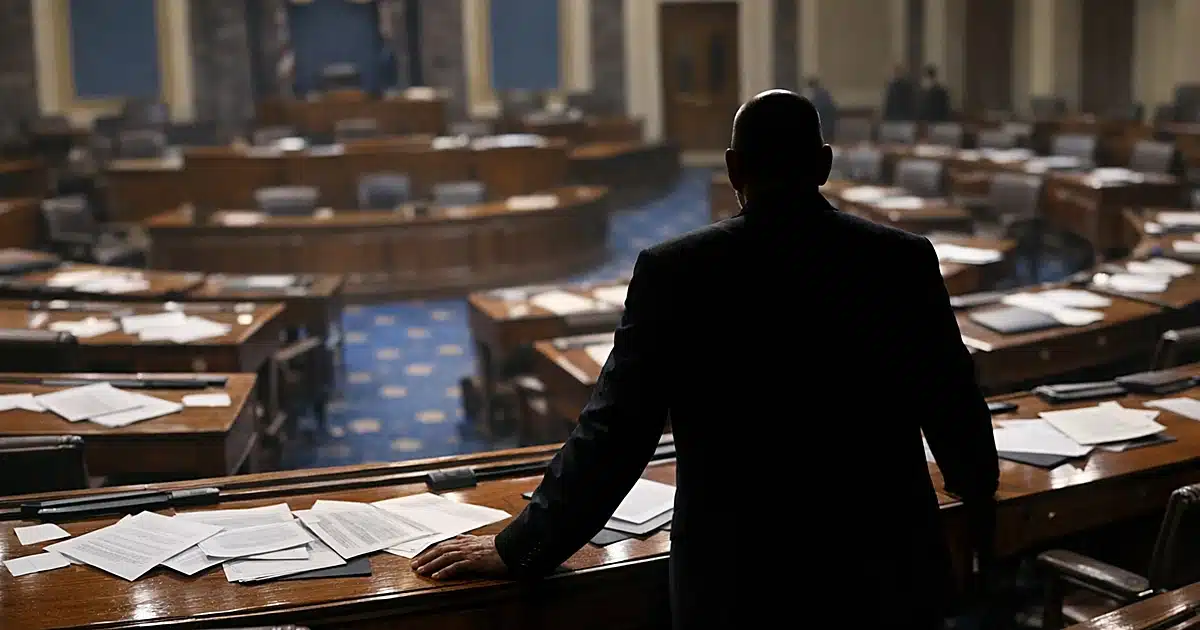 Silhouetted figure standing alone at desk in empty Senate chamber with scattered papers on surrounding desks