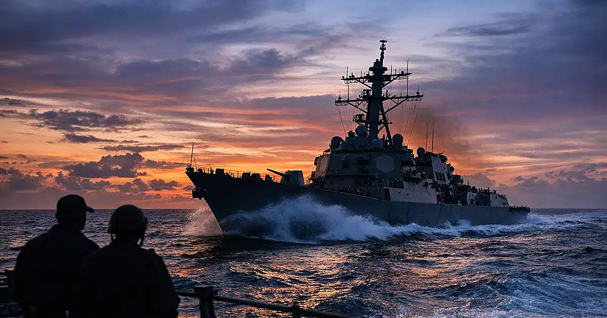 U.S. Navy warship sailing through ocean waters at dusk with dramatic sky