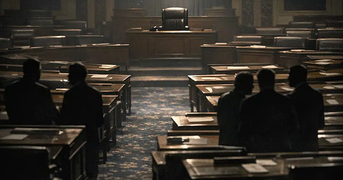 Empty Senate chamber with vacant desk chair spotlit while silhouetted figures converse in aisles