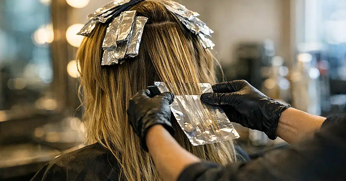 Hairstylist applying foil highlights to long brown hair in upscale salon with natural window lighting