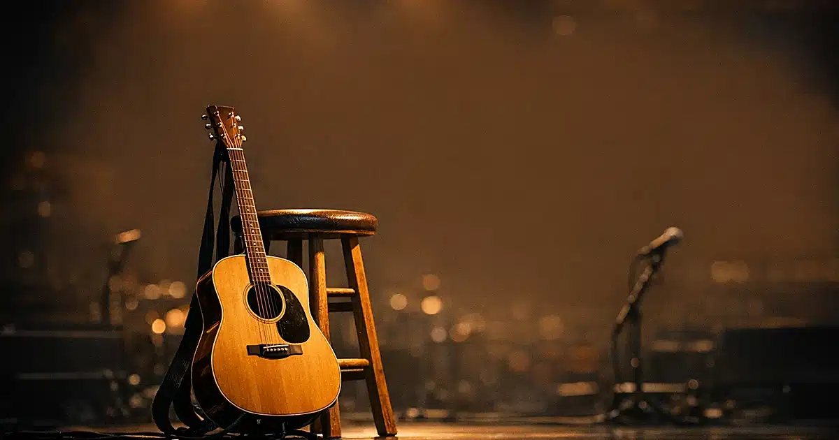 Acoustic guitar on empty concert stage with warm lighting and dark background