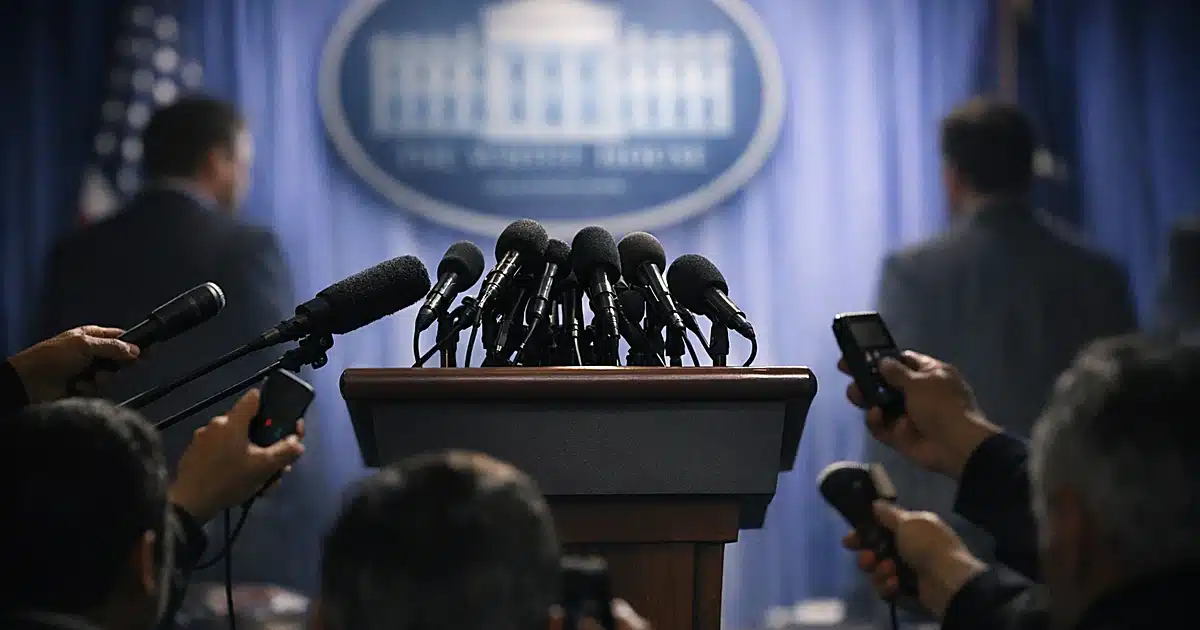 White House press briefing podium with reporters' microphones extended forward in dramatic lighting