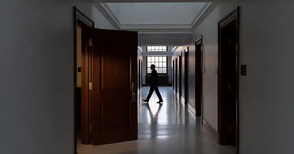 Silhouetted figure walking away down FBI headquarters corridor past open office door