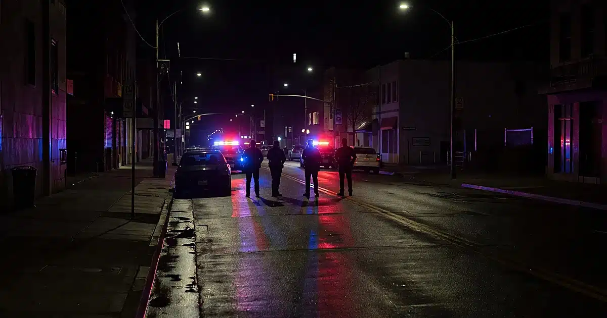 Police patrol cars with flashing lights on wet city street at night with officer silhouettes