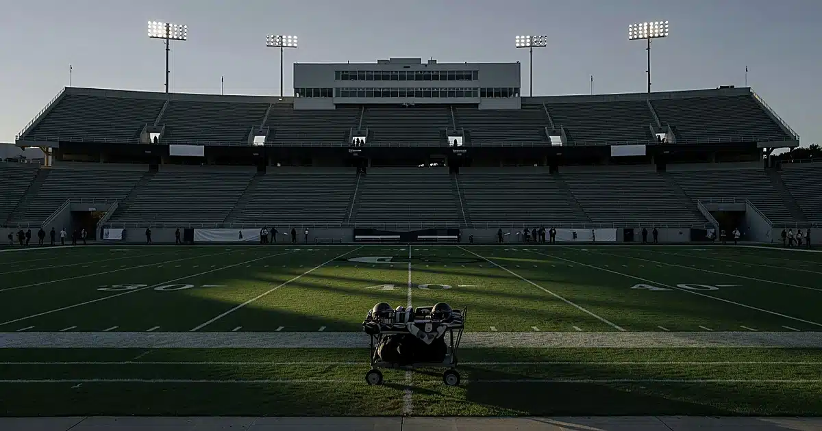 Empty college football stadium at dusk with equipment on sideline and dramatic lighting across the field