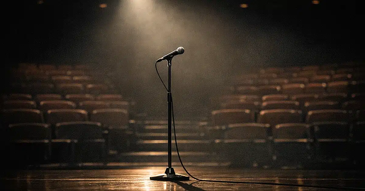 Empty microphone stand under spotlight on dark stage with theater seats fading into background