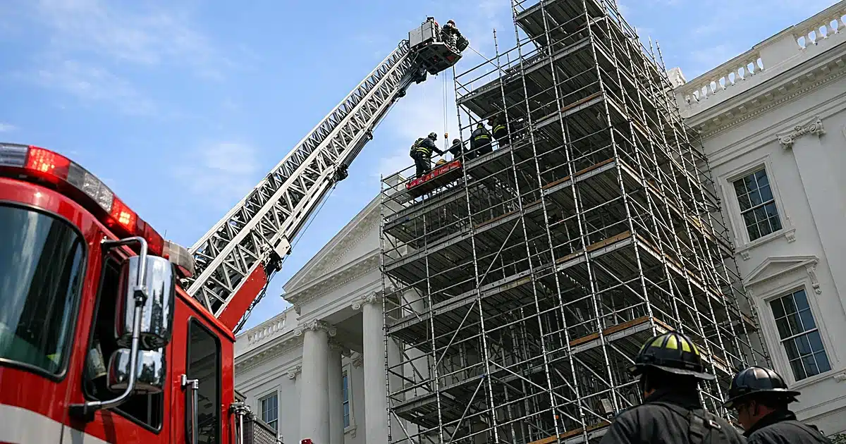 Fire department ladder truck extended toward scaffolding on white government building during rescue operation