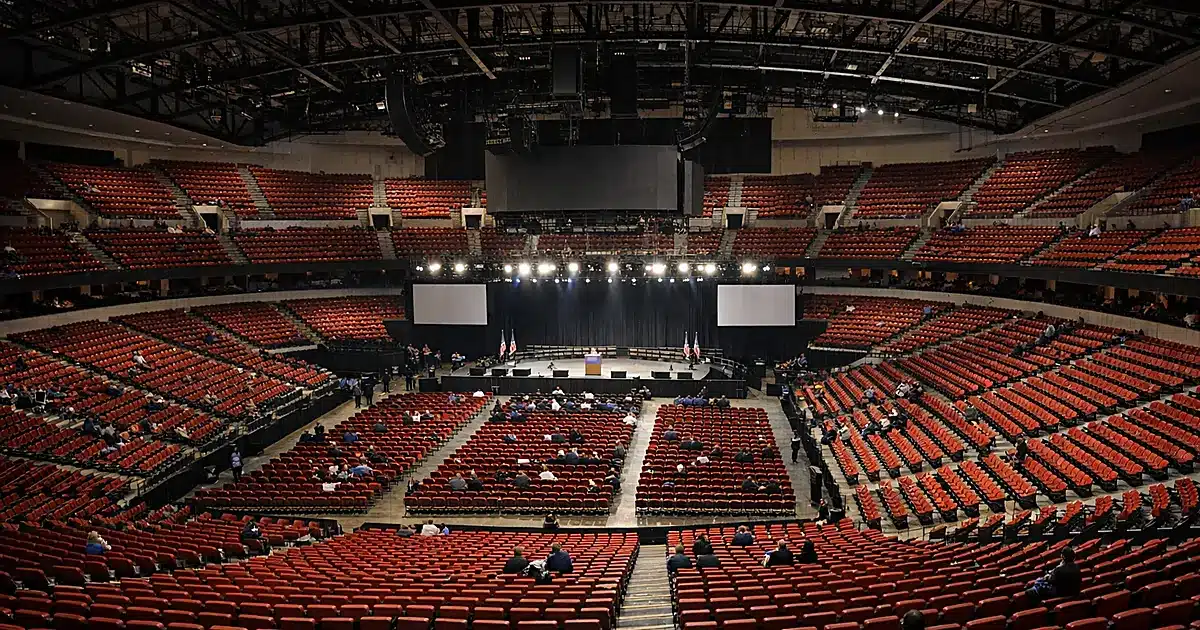 Wide view of large arena interior showing mostly empty seats with scattered attendees under bright lights