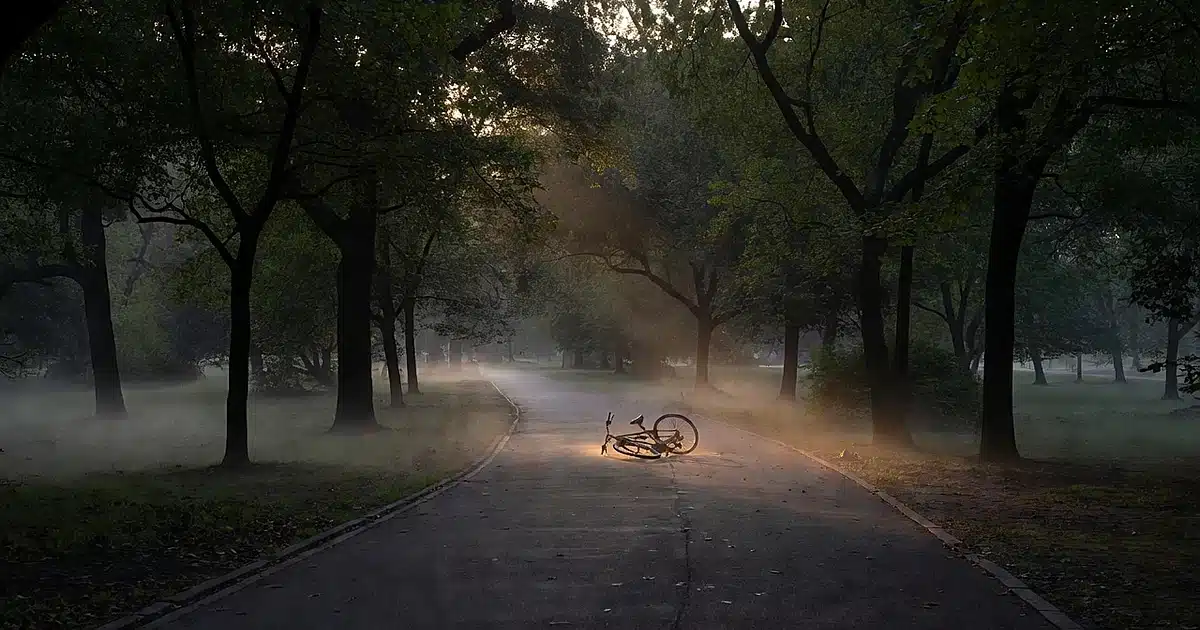 Empty Central Park bicycle path at dawn with fallen bicycle on pavement surrounded by morning mist and trees