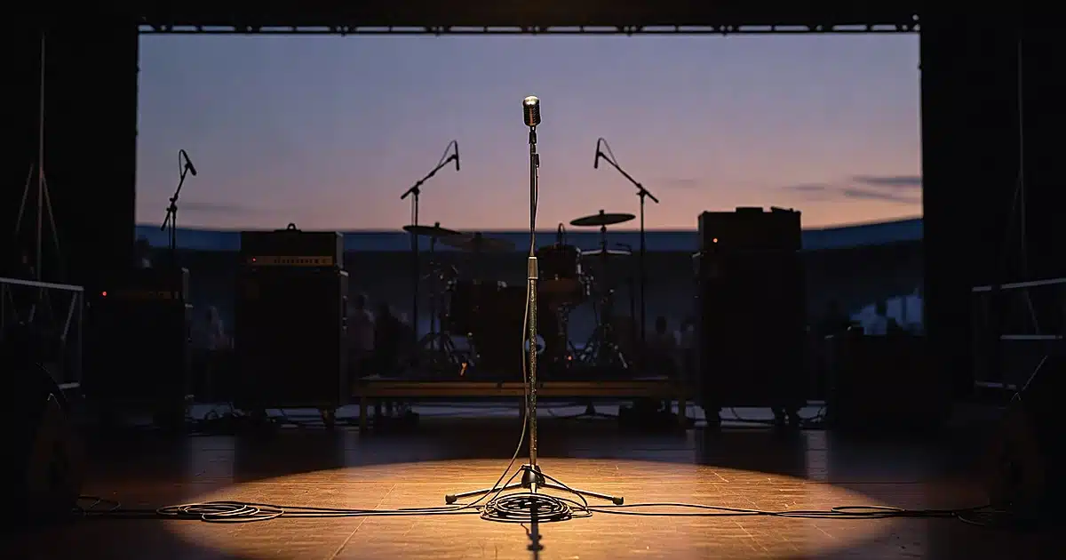 Empty concert stage with microphone stand and equipment silhouettes under stage lights at dusk