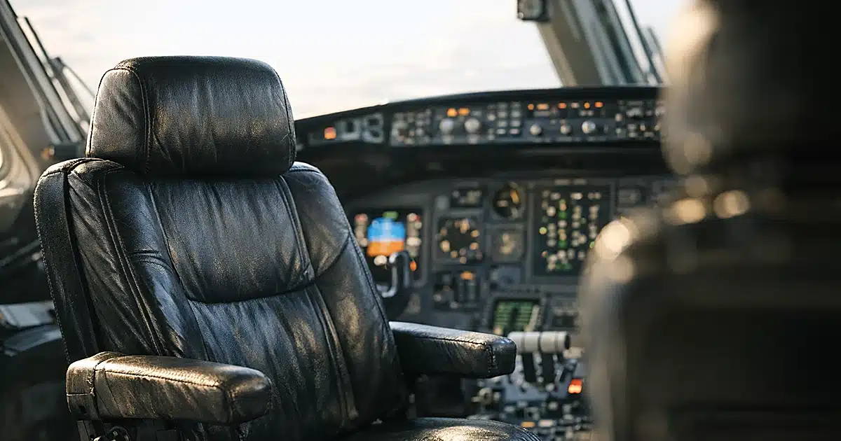Empty airline captain's seat in cockpit with instrument panel in background, afternoon light through windscreen