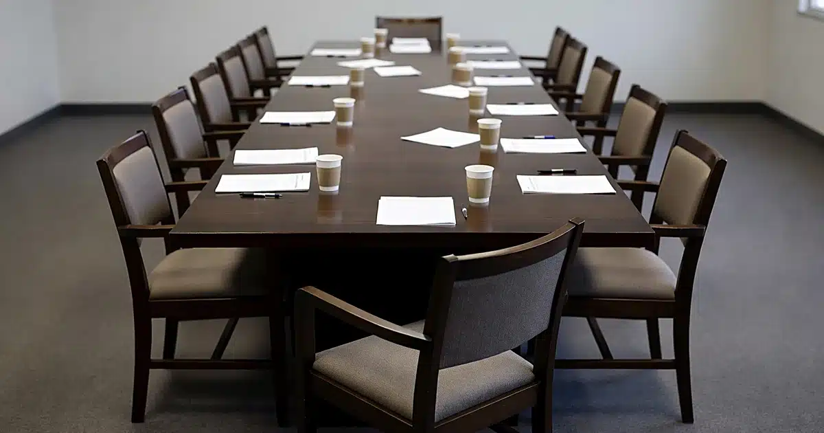 Empty jury deliberation room with wooden table, twelve chairs, and scattered blank papers and coffee cups