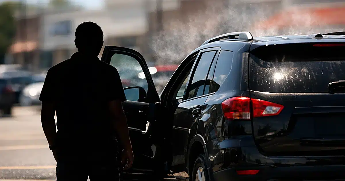Silhouetted figure standing beside parked SUV with rear door open in bright sunlit parking lot