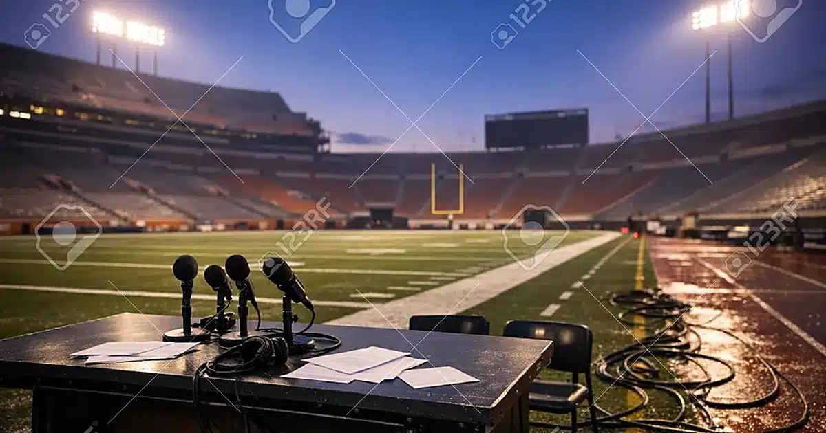 Empty college football stadium at dusk with abandoned broadcast desk and microphones on sideline