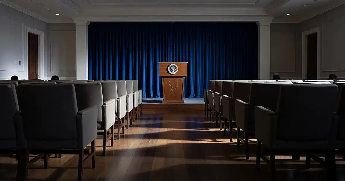 Empty White House press briefing room with vacant chairs and podium under dramatic lighting