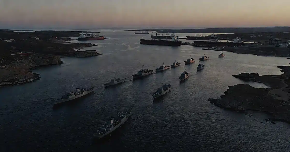 Aerial view of naval vessels blocking a narrow strait with idle tankers waiting at distant ports