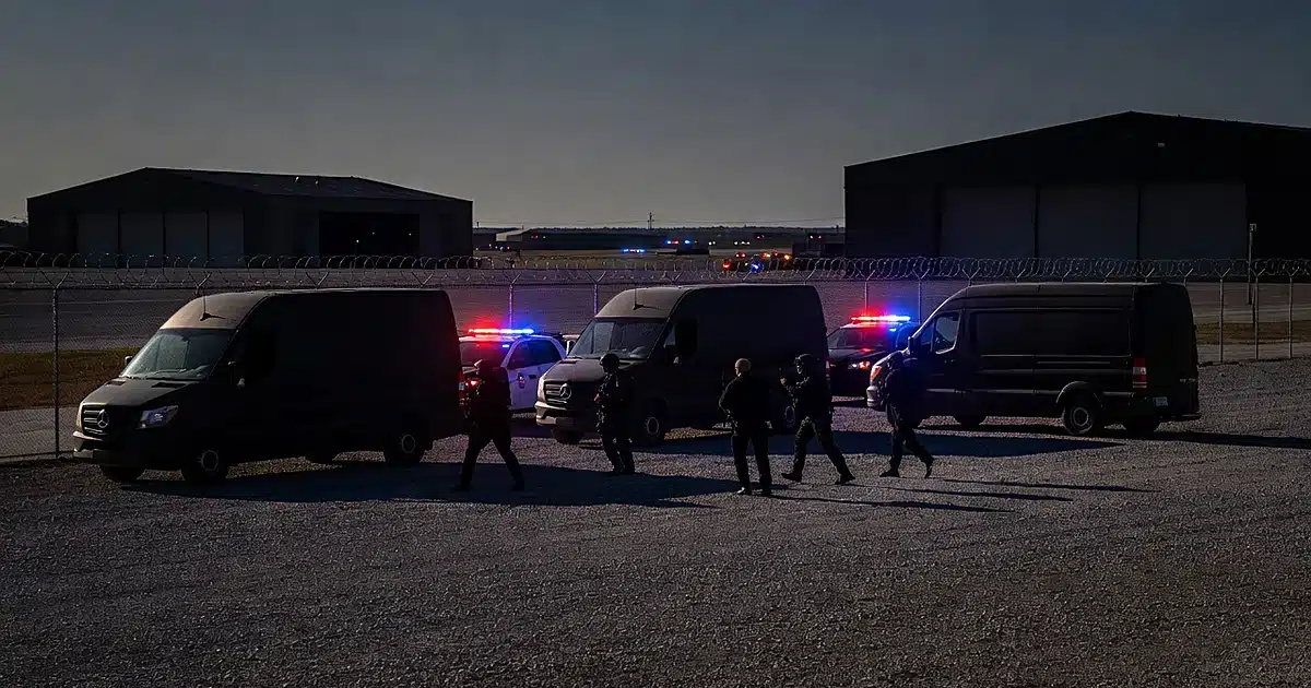Police vehicles with emergency lights at military air base perimeter with vans and officer silhouettes at dusk