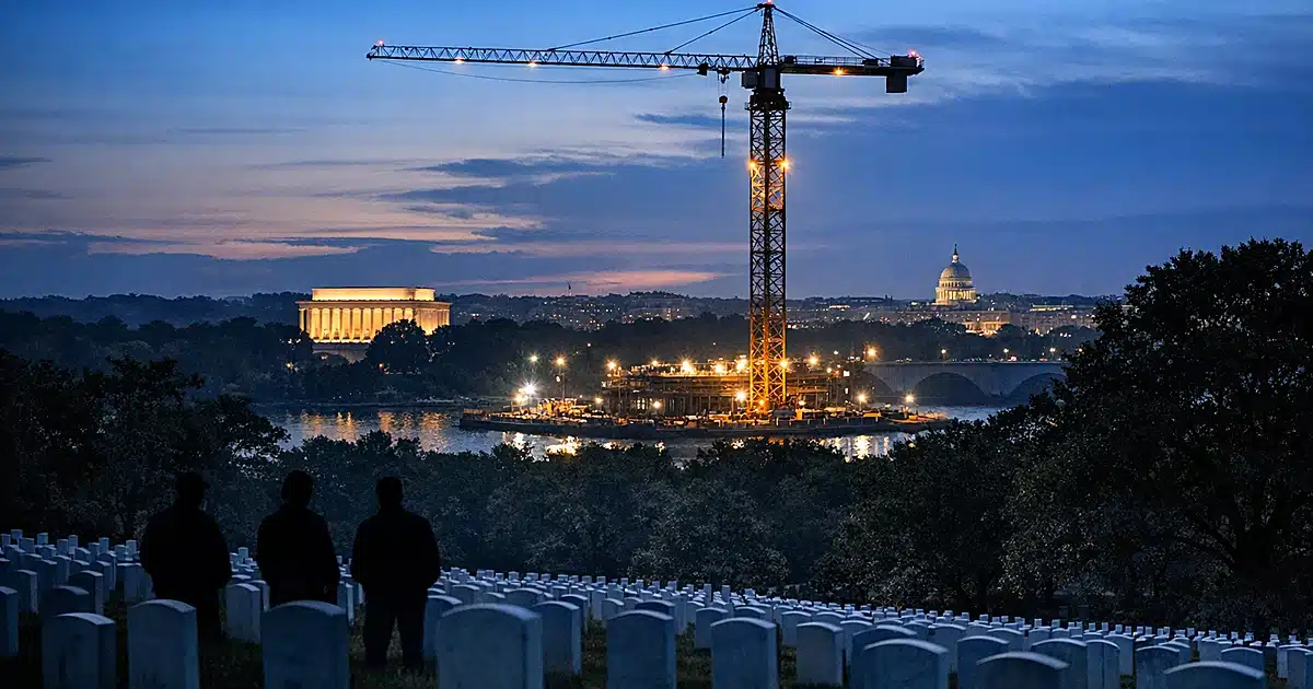 Construction crane rising near Arlington Cemetery headstones at dusk with memorial landscape in background