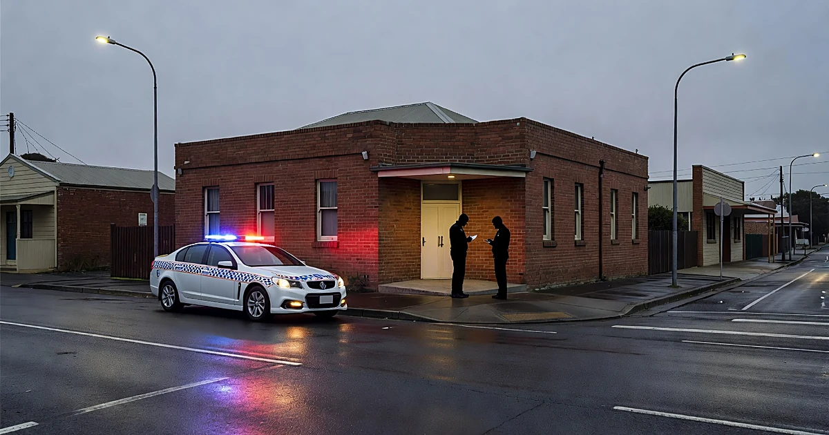 Emergency vehicle lights reflecting on wet pavement outside small-town office building at dusk