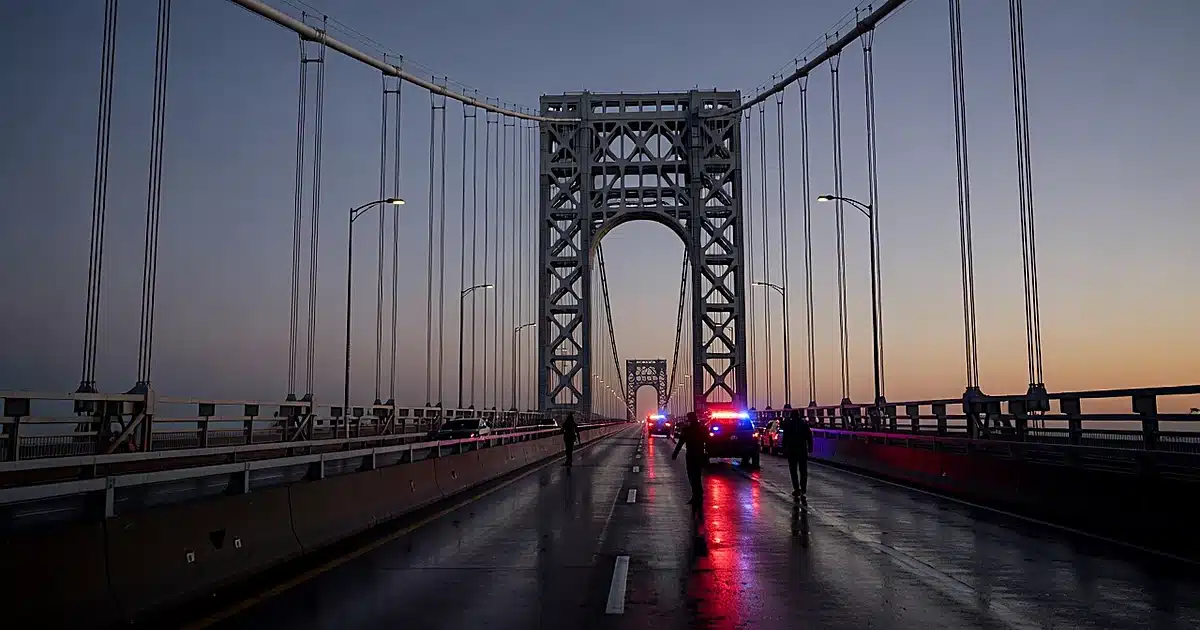 Emergency lights reflecting on wet pavement of George Washington Bridge upper deck at dusk with silhouetted responders