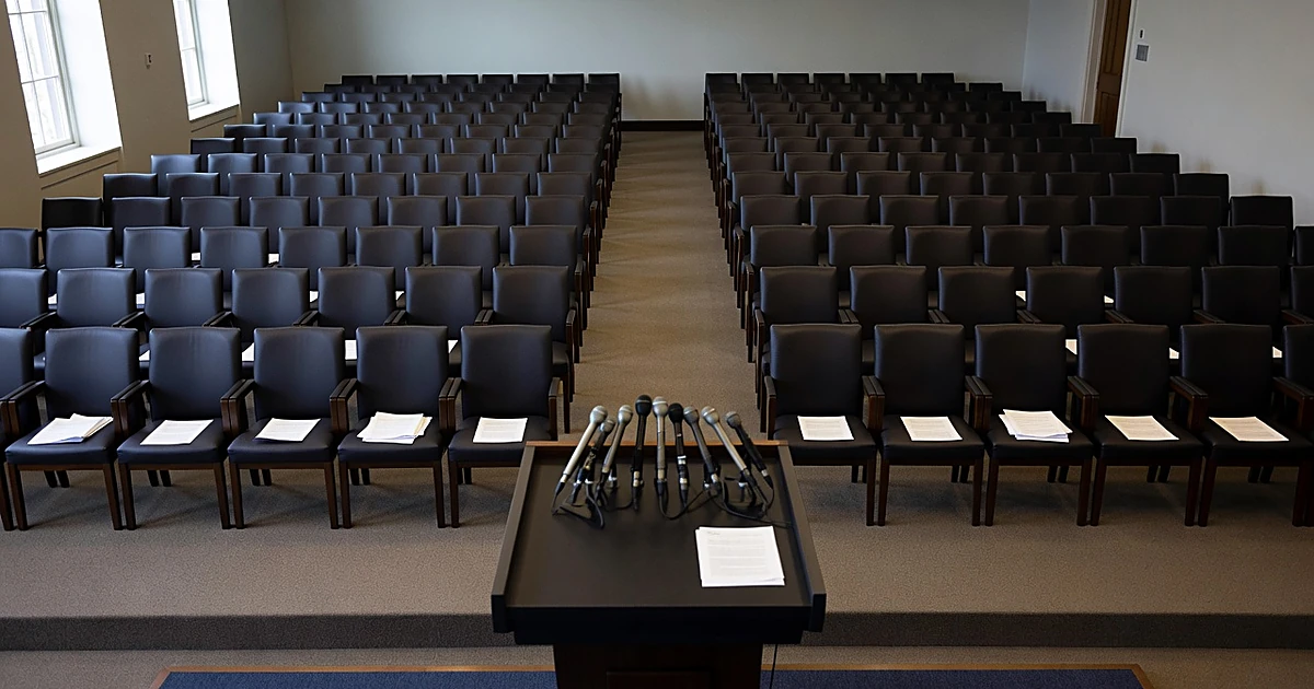 Empty White House press briefing room with vacant chairs facing podium with microphones in neutral daylight