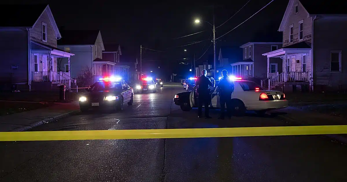 Police vehicles with emergency lights active on residential street at night with crime scene tape in foreground