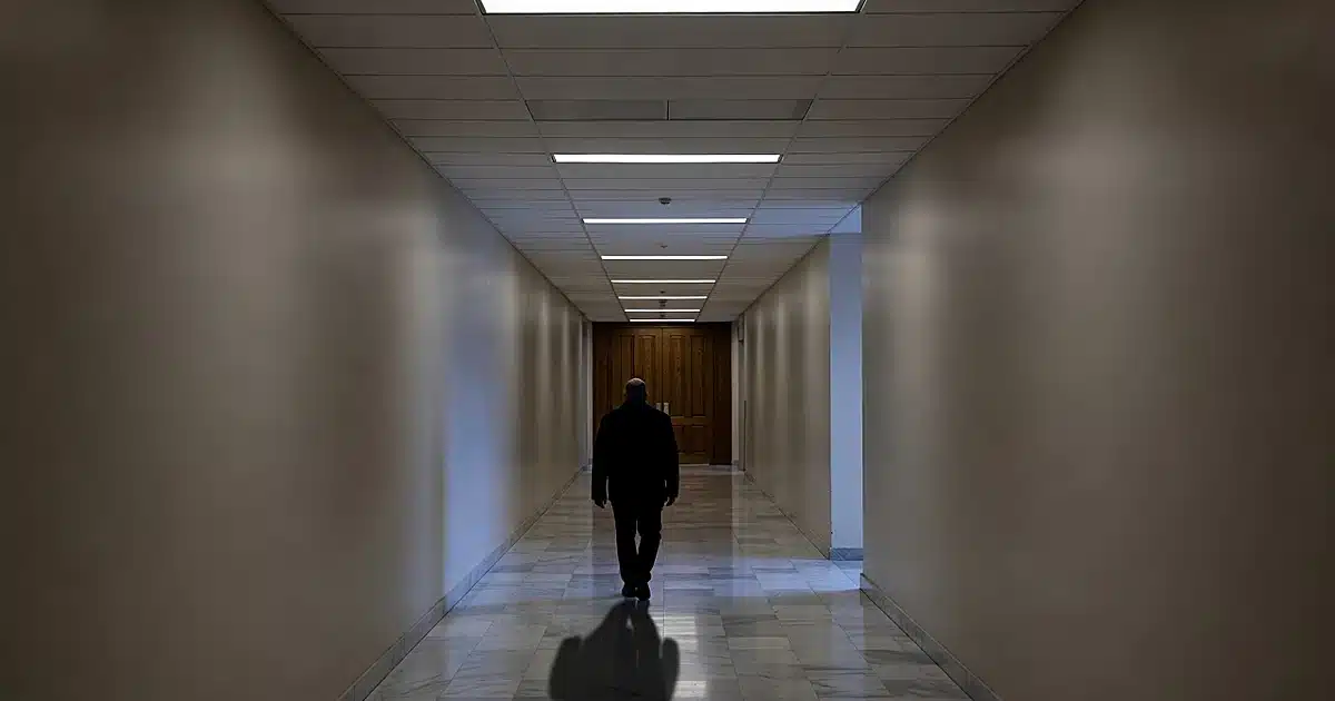 Silhouetted figure walking down empty courthouse hallway toward wooden doors