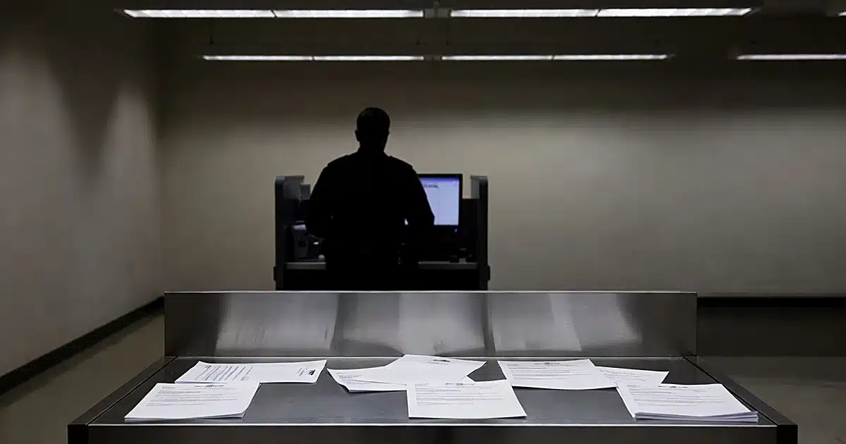 Federal booking station with processing counter and silhouetted officer at computer terminal in background