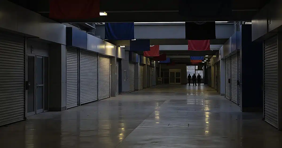 Empty stadium concourse with closed security shutters over storefronts at dusk