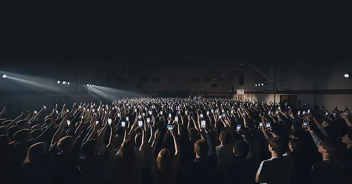 Silhouetted crowd with raised phones at indoor political rally in large gymnasium venue