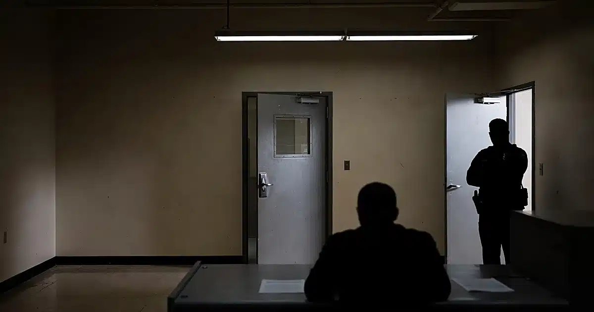 Police booking station interior with security door and silhouetted figures at processing desk