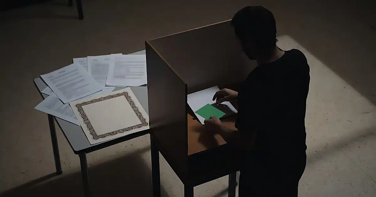 Silhouette at voting booth holding green card with scattered documents and birth certificate on nearby table