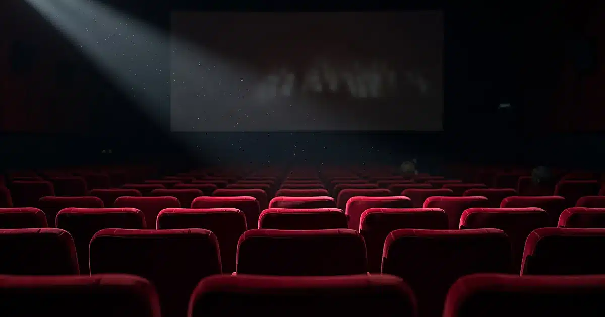 Empty movie theater with projection light beam cutting through darkened rows of red velvet seats