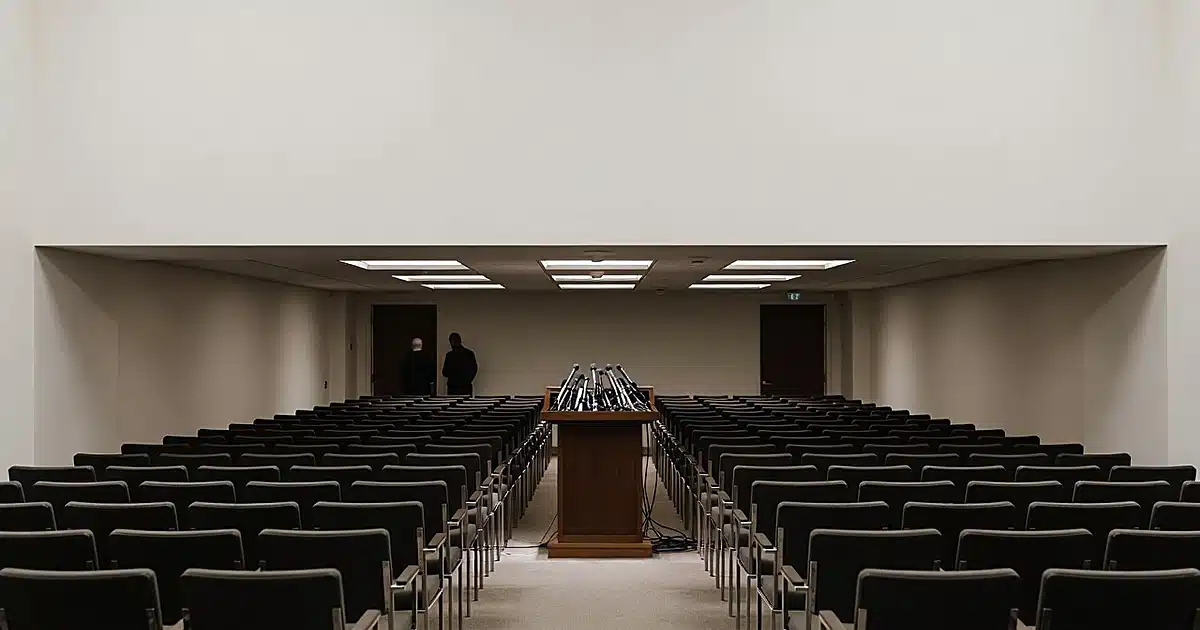 Empty White House press briefing room with podium and microphones, figures silhouetted in background