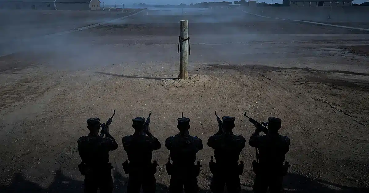 Military firing squad formation at dawn on Army rifle range with soldiers as silhouettes facing execution post