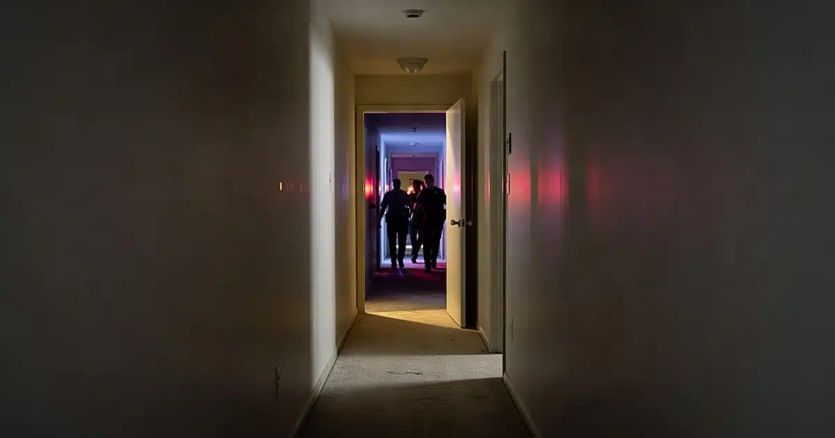 Dark apartment building hallway with emergency lights and silhouetted first responders in motion at night